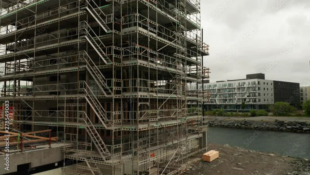 Aerial of New Real Estate Construction Apartments and Offices Building by River Canal With Metal Workers Platforms Aerial of New Real Estate Construction Apartments and Offices Building by River Canal With Metal Workers Platforms