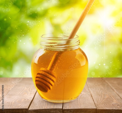 Fresh sweet honey with wooden honey dipper in glass jar isolated on white background