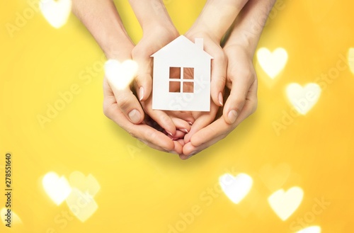 Hands holding house model on white wooden background