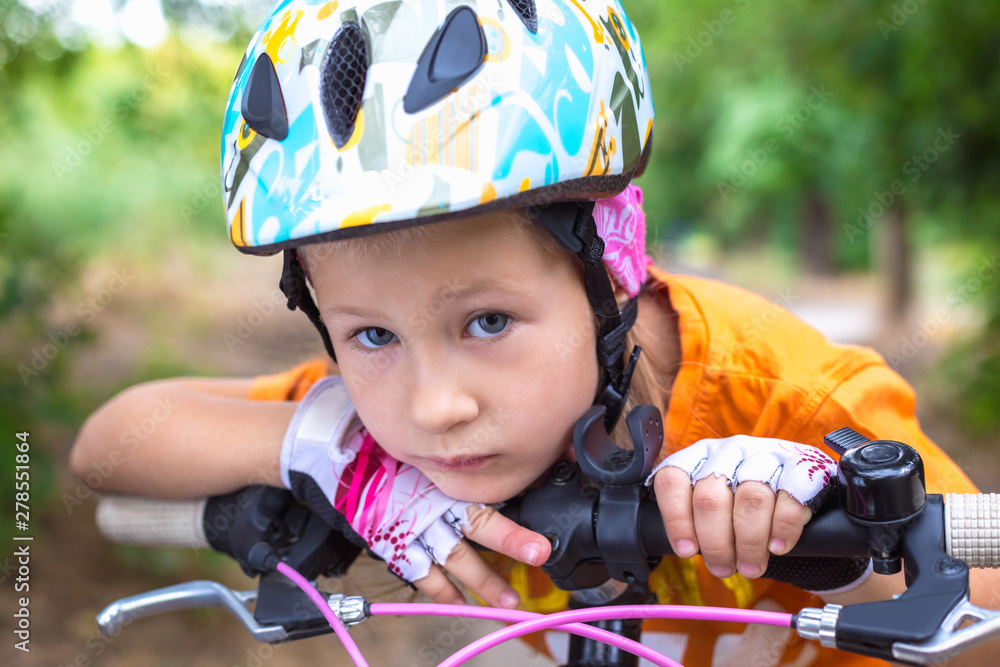 Cute little sad girl in a helmet with a bike in the summer Cute little sad girl in a helmet with a bike in the summer