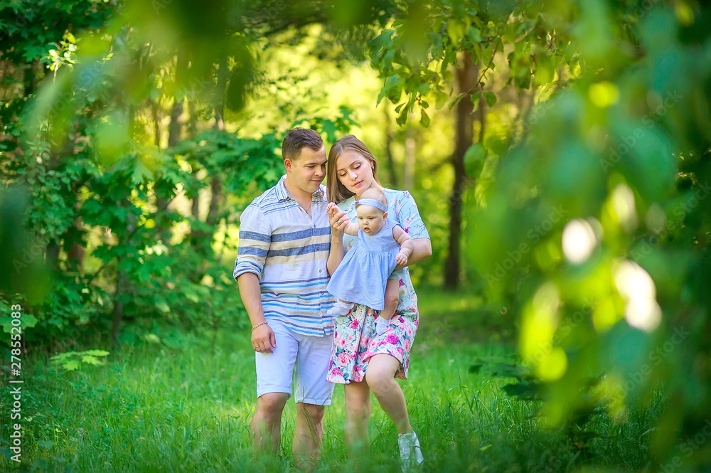 Fototapeta premium Friendly family. parents walk with their little daughter in a beautiful summer park at sunset. people concept.