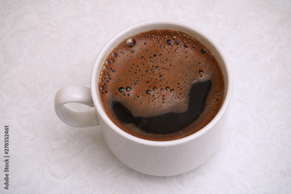 Hot black coffee with thick froth in a white cup on white table background Hot black coffee with thick froth in a white cup on white table background