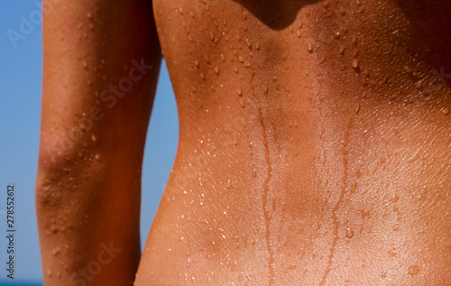 Beautiful girl shows her tanned slim back or spine, still wet with water drops from bathing in the ocean.