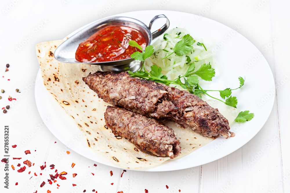 Close up view on grilled Lyulya kebab or Lule kebab. shashlik or barbecue meat on pita. Shish kebab, traditional georgian cuisine food. Copy space for design. Meat food with red sauce Close up view on grilled Lyulya kebab or Lule kebab. shashlik or barbecue meat on pita. Shish kebab, traditional georgian cuisine food. Copy space for design. Meat food with red sauce
