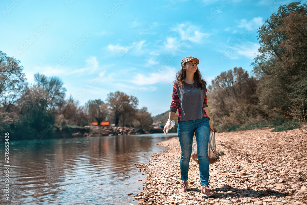A young woman volunteer collects garbage along the river. The concept of earth day and ecology and environmental conservation. Tint and copy space A young woman volunteer collects garbage along the river. The concept of earth day and ecology and environmental conservation. Tint and copy space