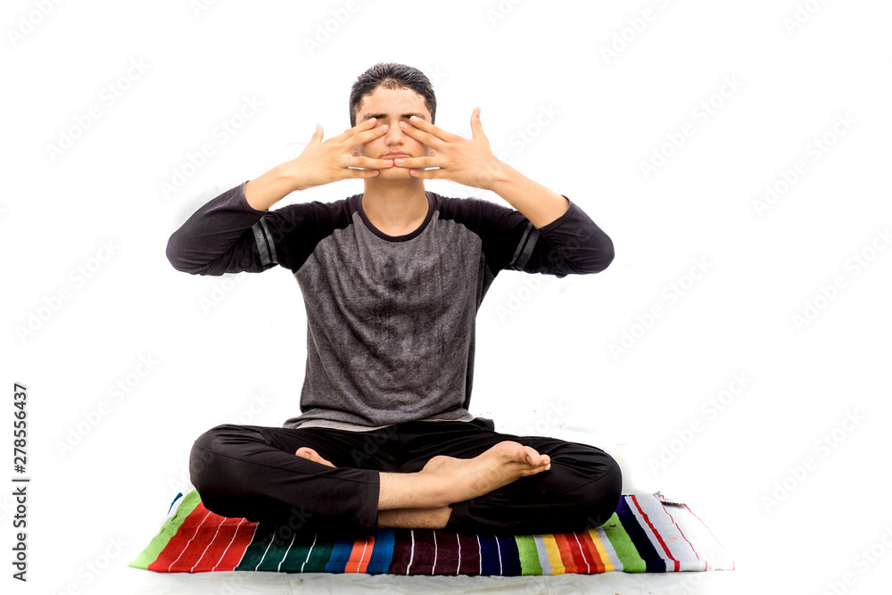 A young caucasian teenager wearing activewear pants and black colored  t-shirt and performing Bhramari pranayama or human humming bee breathing  exercise yoga isolated on white.On colorful yoga mat. Stock Photo