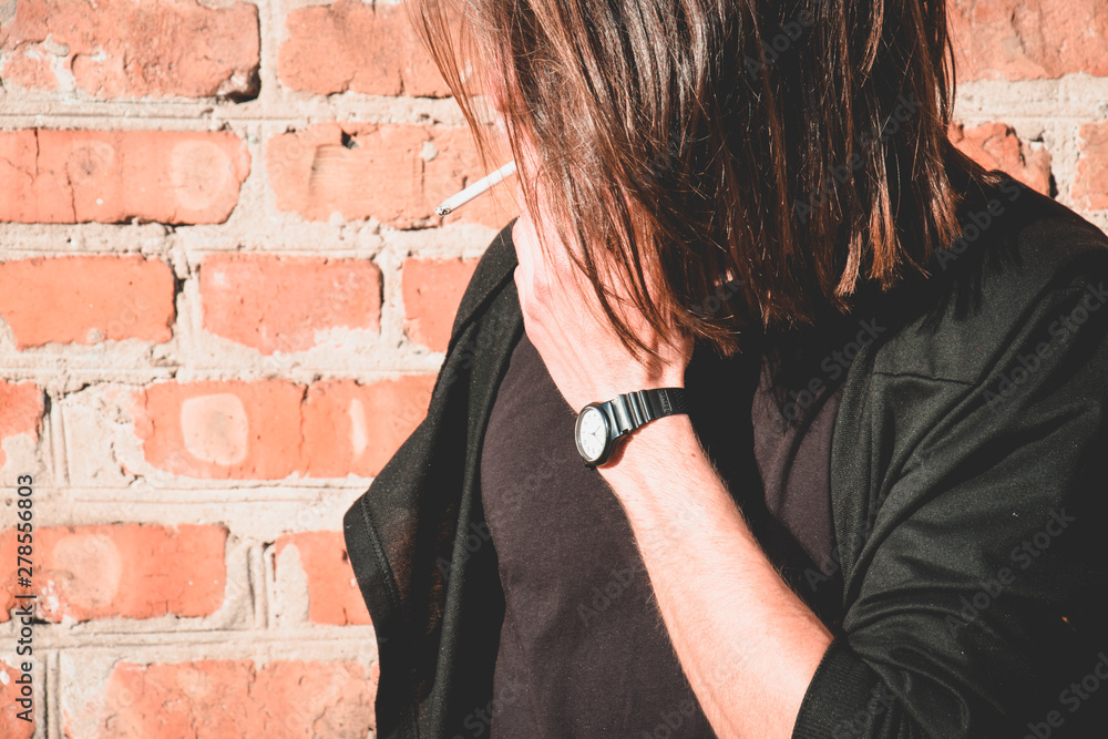A young man with a cigarette near a bricks wall. Place for text. A young man with a cigarette near a bricks wall. Place for text.