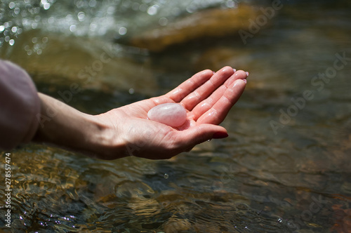 Woman holding in hand a yoni egg. Rose quartz crystal egg on river background. Female health concept
