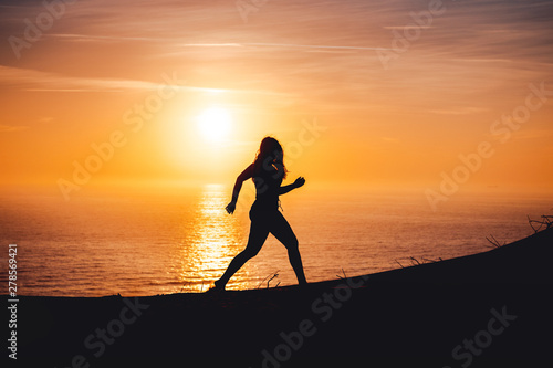 Side view of a active sport woman running at the beach with evening summer sunset light on relax sea vacations. Rubjerg Knude Lighthouse, Lønstrup in North Jutland in Denmark, Skagerrak, North Sea