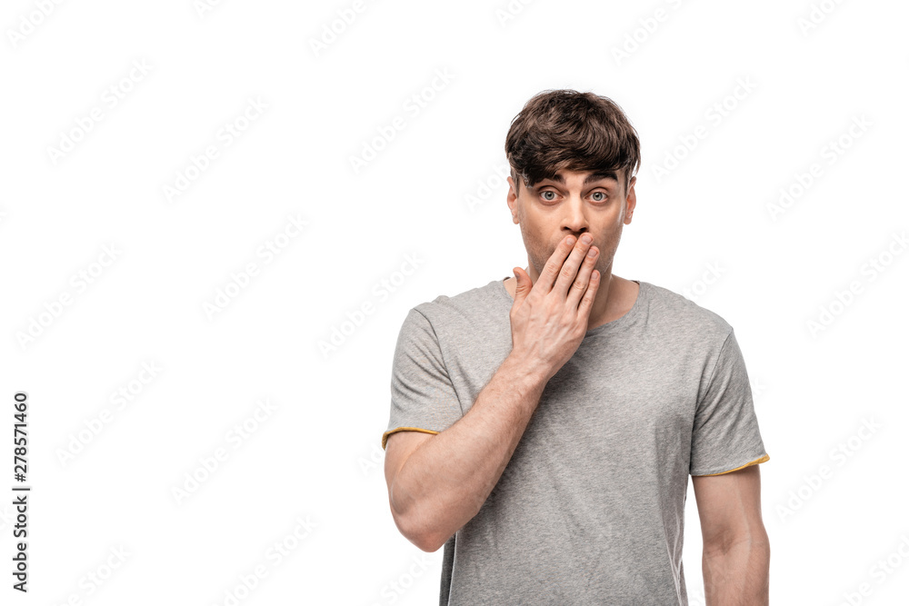 shocked young man looking at camera while covering mouth with hand isolated on white shocked young man looking at camera while covering mouth with hand isolated on white