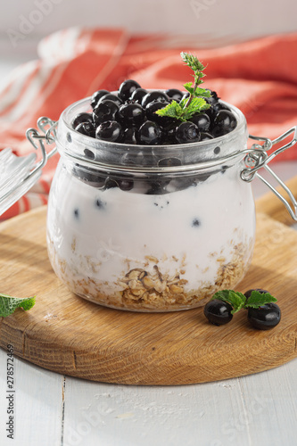 Granola yogurt in glass jar on a wooden board in home kitchen