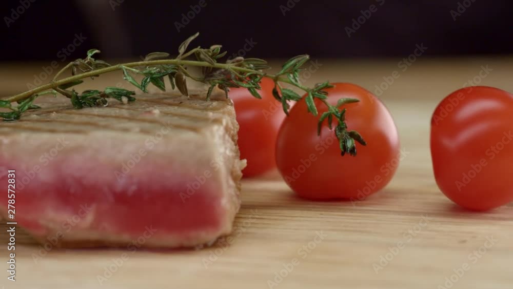 Grilled rare tuna steak on a wooden board with cherry tomatoes and thyme.