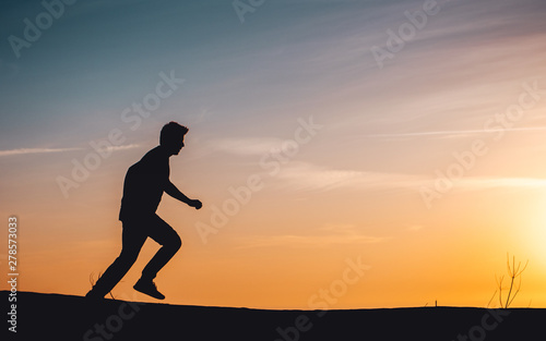 Side view of a active sport athlete man jumping and having fun in wide endless sand dunes at colorful, amazing sunset evening light. Lokken, Lønstrup in North Jutland in Denmark, Skagerrak, North Sea © Ricardo