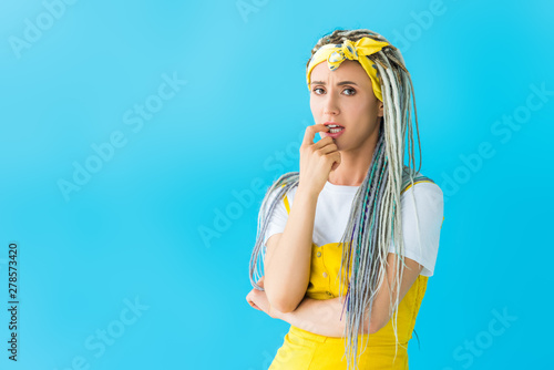 worried girl with dreadlocks biting finger isolated on turquoise