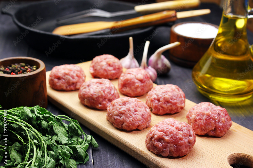 close up raw meatballs on a cutting board on a background of a bamboo mat with garlic and parsley