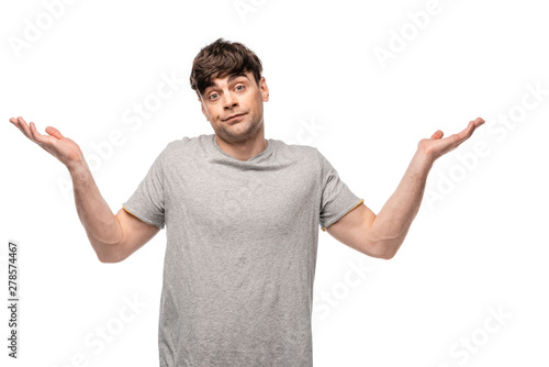 discouraged young man showing shrug gesture while looking at camera isolated on white