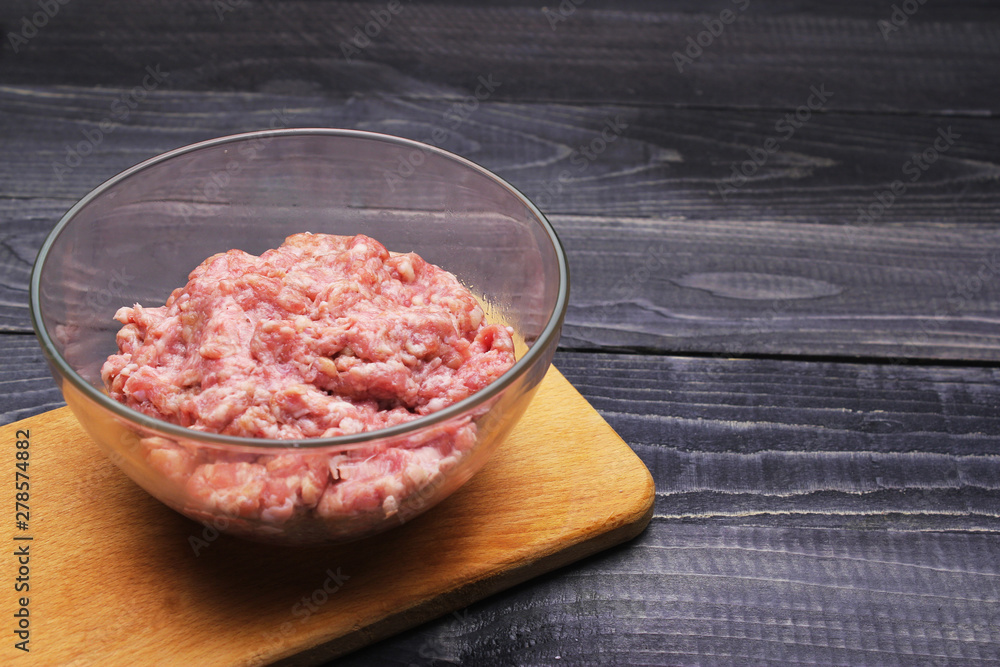 raw minced meat in glass bowl on cutting board on black wooden table top surface raw minced meat in glass bowl on cutting board on black wooden table top surface