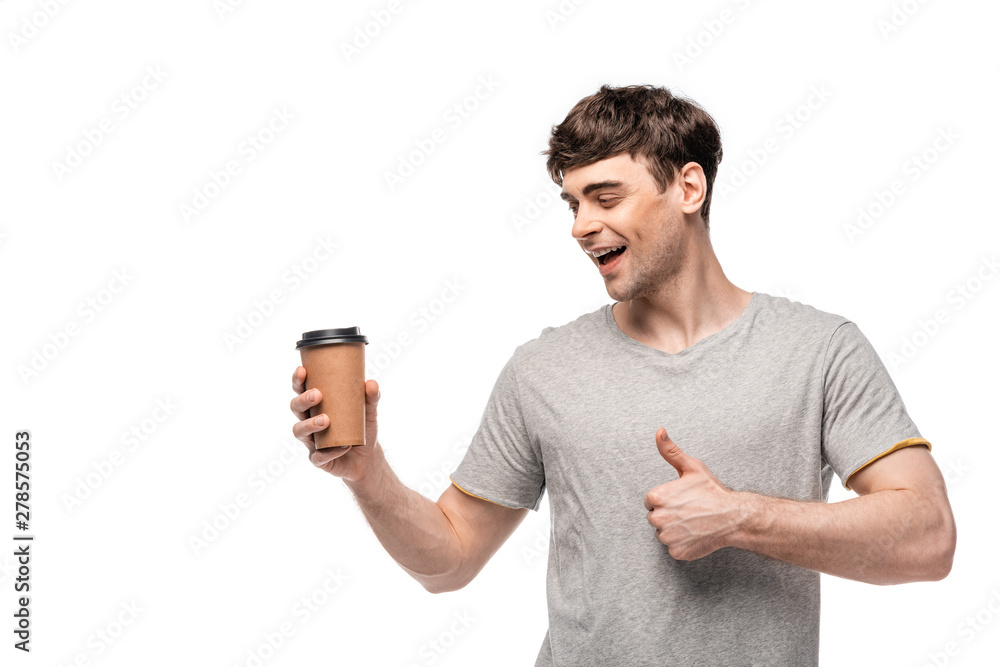 smiling handsome man looking at disposable cup and showing thumb up isolated on white smiling handsome man looking at disposable cup and showing thumb up isolated on white