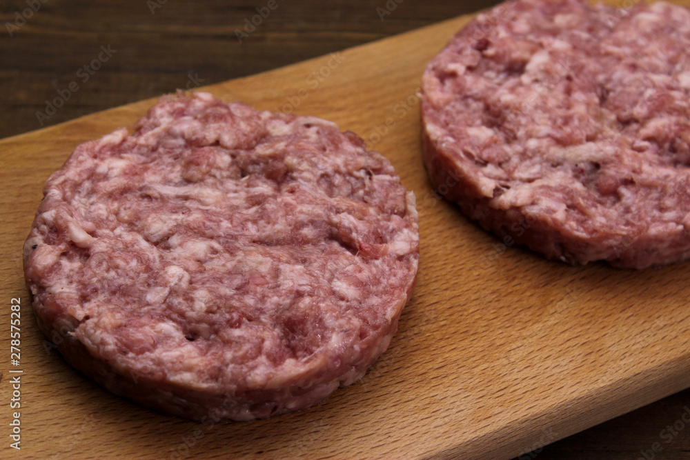 Burger. Ground meat. Close up fresh raw minced beef steak burgers served on cutting board on empty dark wooden table top Burger. Ground meat. Close up fresh raw minced beef steak burgers served on cutting board on empty dark wooden table top