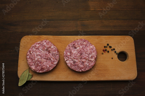 Burger. Ground meat. Fresh raw minced beef steak burgers with spices served on cutting board on empty dark wooden table top flat lay