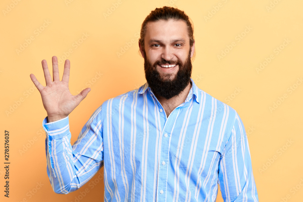 Positive awesome handsome man dressed in striped shirt and saying hi, waving his hand, body language, isolated yellow background. studio shot Positive awesome handsome man dressed in striped shirt and saying hi, waving his hand, body language, isolated yellow background. studio shot