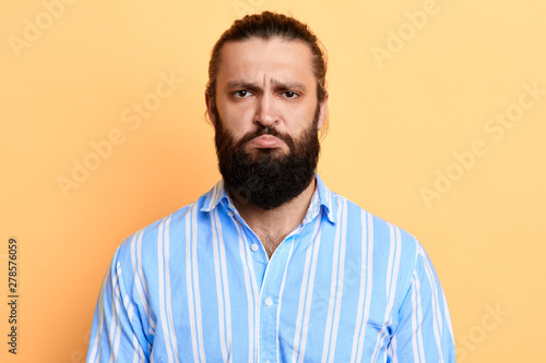 Nervous doubtful handsome bearded man in stylish shirt frowning his eyebrow, having puzzled look going to make serious decision.isolated yellow backgroun. studio shot © the faces