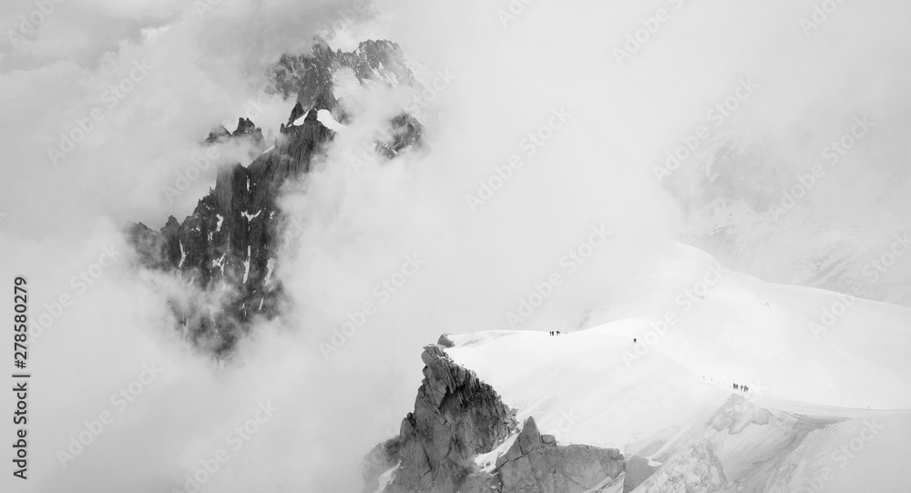 Dramatic panoramatic view of climbers in French Alps climbing among low clouds