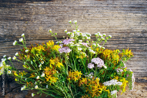 Bouquet of wild flowers on old wooden background, soft focus. Alternative medicine. White yarrow flowers, St. John's Wort flowers, camomile 