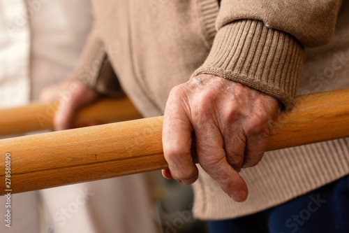 Detail of aged human hands grabbing parallel rehabilitation bars.