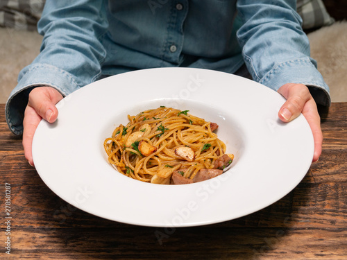 A female uses hands to holding and handing a dish of Spicy spaghetti with pork sausage and garlic in white bowl, Italian cuisine