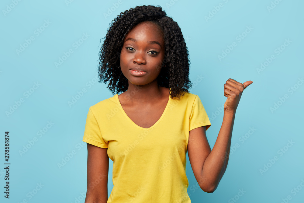 Beautiful young American woman wearing stylish T-shirt smiling and pointing to the side with thumb up.close up photo. way, direction concept Beautiful young American woman wearing stylish T-shirt smiling and pointing to the side with thumb up.close up photo. way, direction concept