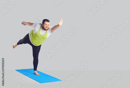 A funny fat man does yoga exercises on a mat on a background.