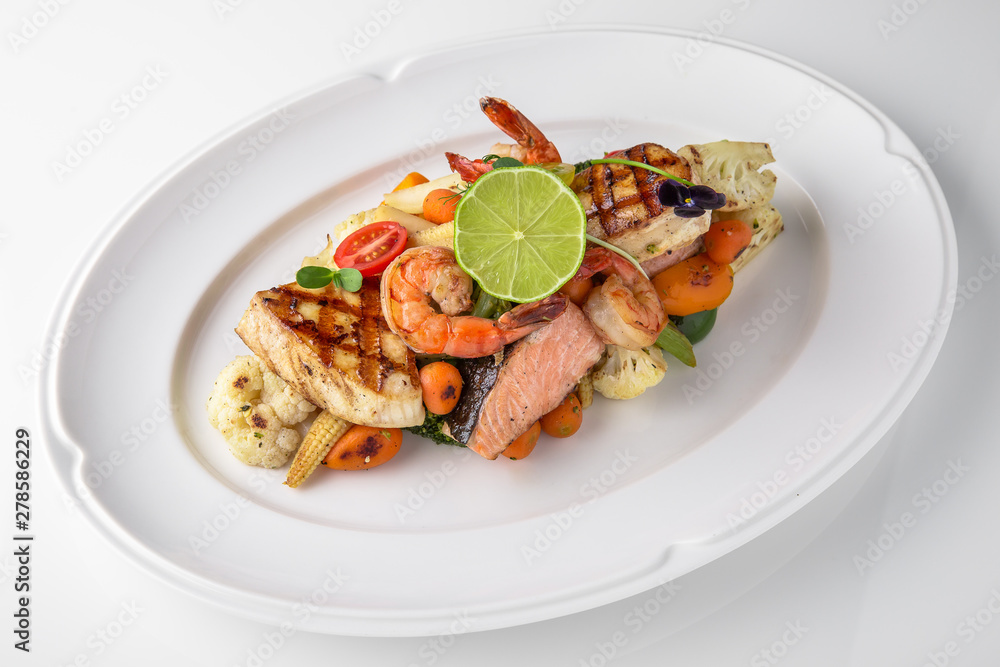 Luxurious seafood salad with shrimp, octopus, squid, fish, lime, cherry tomatoes, grilled vegetables and greens Banquet festive dishes. Fine dining restaurant menu. White background. Luxurious seafood salad with shrimp, octopus, squid, fish, lime, cherry tomatoes, grilled vegetables and greens Banquet festive dishes. Fine dining restaurant menu. White background.