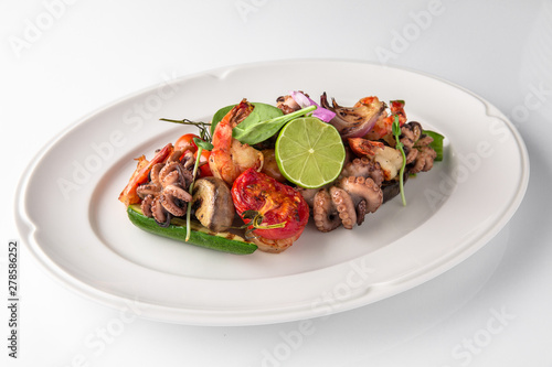 Luxurious seafood salad with shrimp, octopus, squid, fish, lime, cherry tomatoes, grilled vegetables and greens Banquet festive dishes. Fine dining restaurant menu. White background.