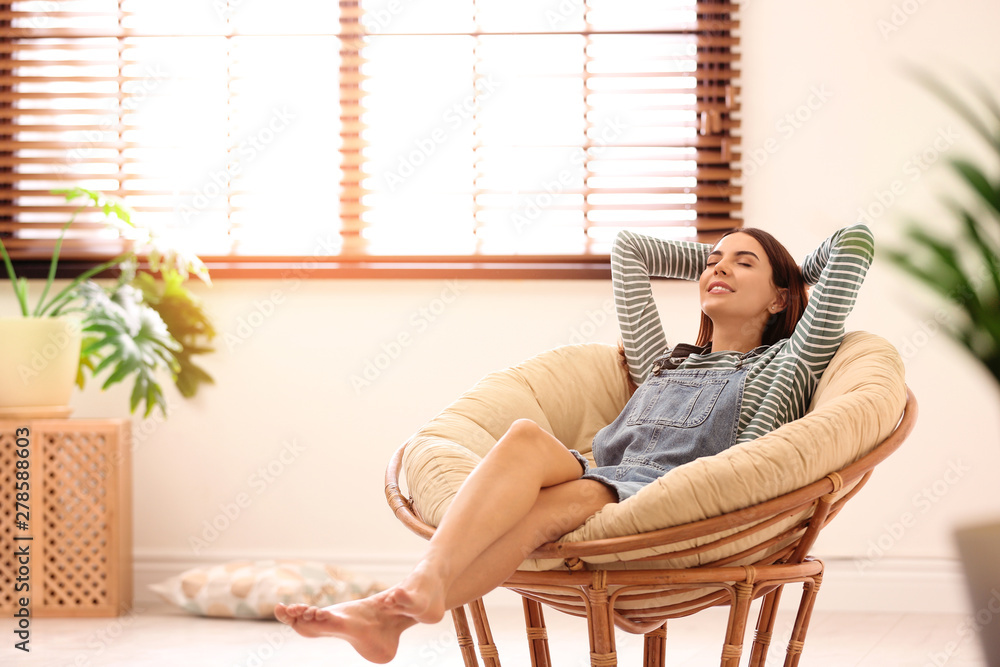 Young woman relaxing in papasan chair near window with blinds at