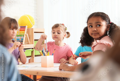 Adorable children drawing together at table indoors. Kindergarten playtime activities