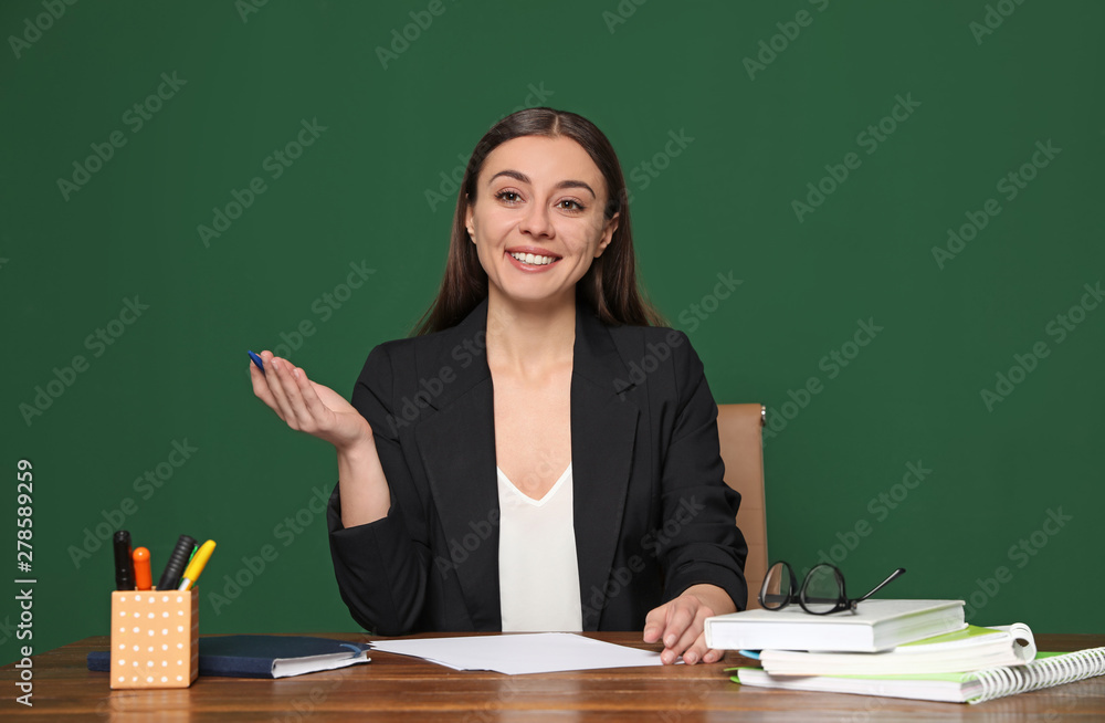Portrait of young teacher at table against green background Portrait of young teacher at table against green background