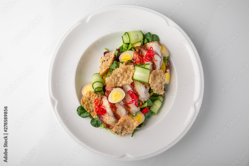 Delicious salad of smoked eel, fresh vegetables, quail eggs and crispy chips. Nutritious healthy dish. Banquet festive dishes. Gourmet restaurant menu. White background.