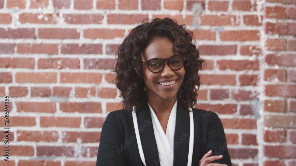 Portrait Of Smiling Businesswoman Wearing Glasses Standing Against Brick Wall In Modern Office Portrait Of Smiling Businesswoman Wearing Glasses Standing Against Brick Wall In Modern Office