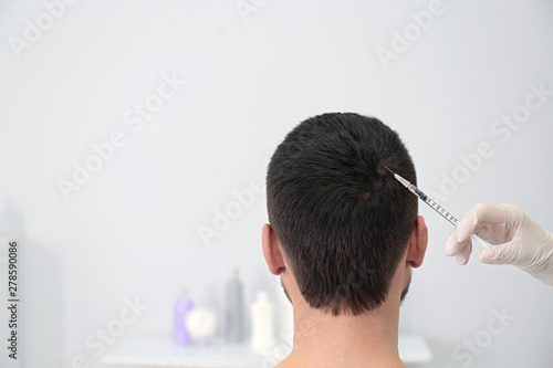 Man with hair loss problem receiving injection in salon. Space for text