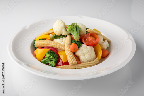 Fresh boiled vegetables: baby carrots, small corn dill, broccoli, cherry tomatoes, sweet peppers. Nutritious healthy dish. Banquet festive dishes. Gourmet restaurant menu. White background.