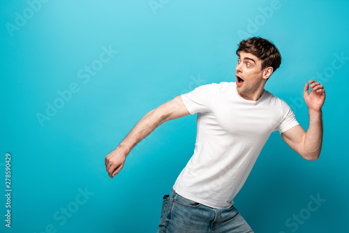 scared young man running away and looking back on blue background