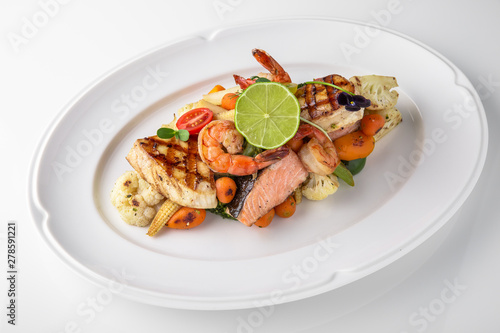 Luxurious seafood salad of shrimp, grilled salmon fillet, sea bream, grilled vegetables and lime. Banquet festive dishes. Fine dining restaurant menu. White background.