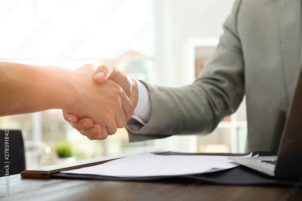 Business partners shaking hands at table after meeting in office, closeup