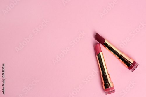 Bright lipsticks in gold tubes on pink background, flat lay. Space for text