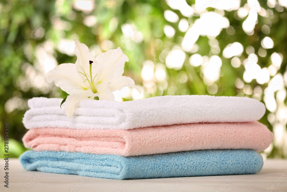 Pile of fresh towels and flower on table against blurred background, space for text Pile of fresh towels and flower on table against blurred background, space for text