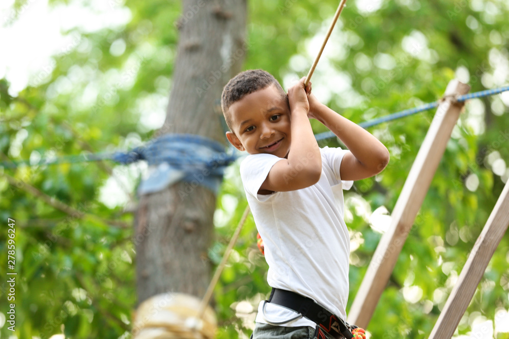 Little African-American boy climbing in adventure park. Summer camp - obrazy, fototapety, plakaty 
