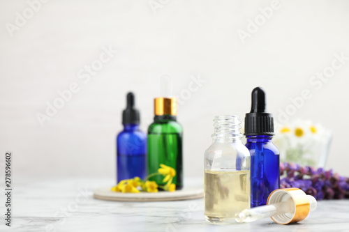 Bottles of different essential oils and wildflowers on marble table, space for text