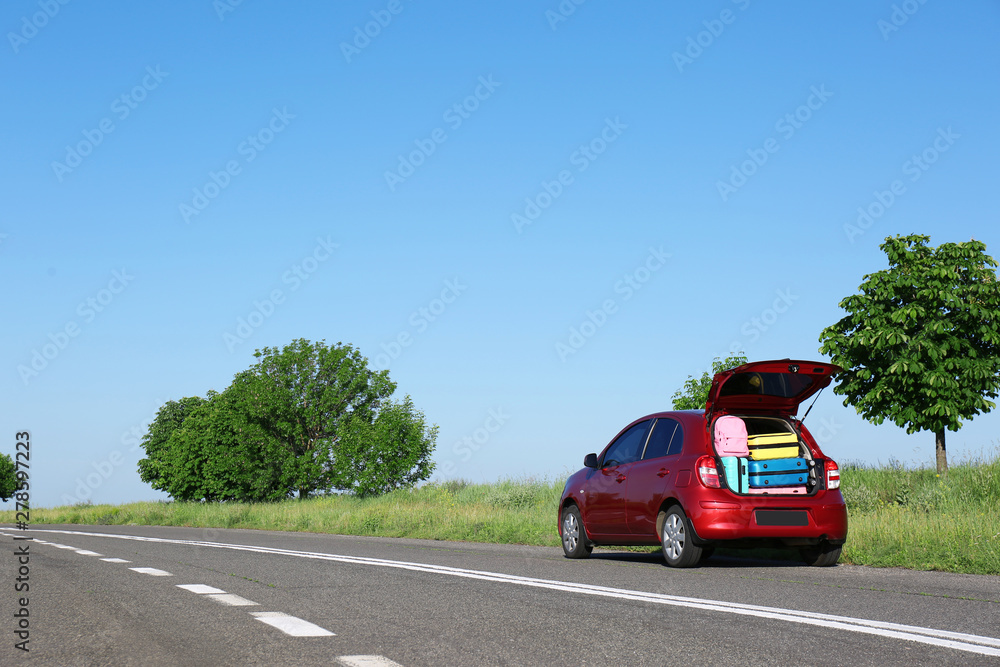 Family car with open trunk full of luggage on highway. Space for text