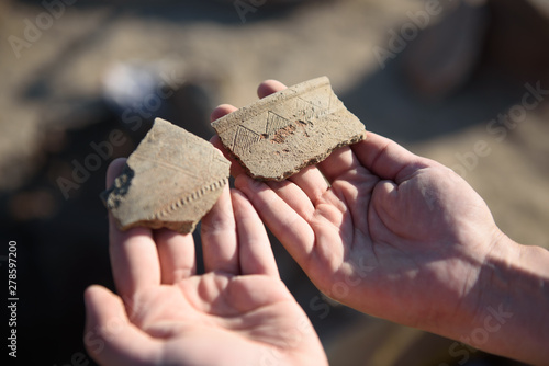An archaeologist at an archaeological site shows fragments of ancient pottery in the hands of photo